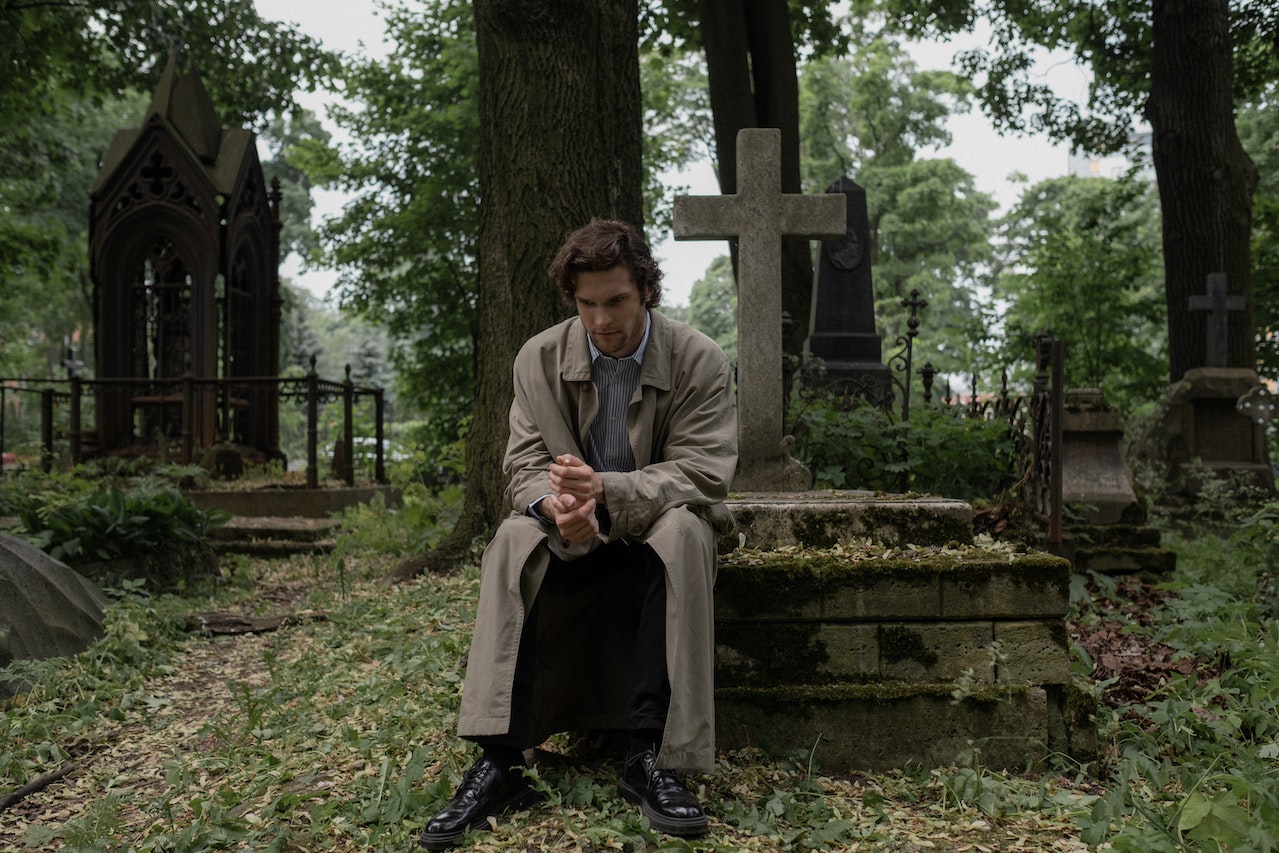 A Man in a Trench Coat Sitting on a Grave