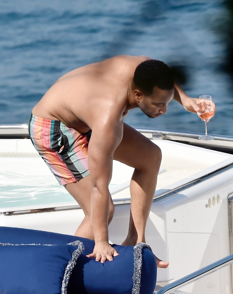 John Legend wearing swimming trunks and holding a glass of wine