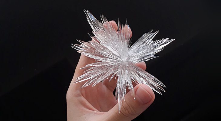 Transparent homegrown needle-shaped crystal in a hand