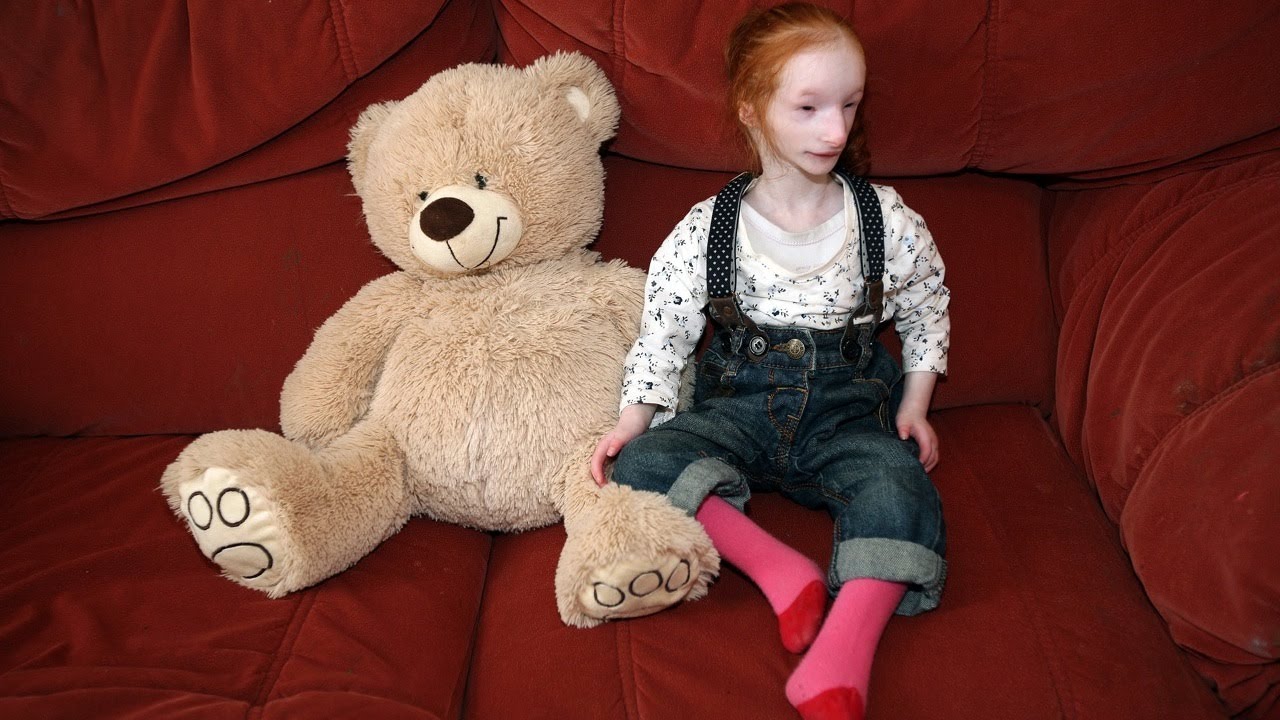 Charlotte Garside and a bear stuffed toy on a red sofa