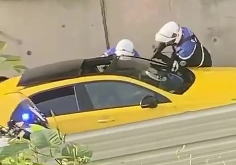 Police officers pointing a gun at the teen driver of a yellow car.