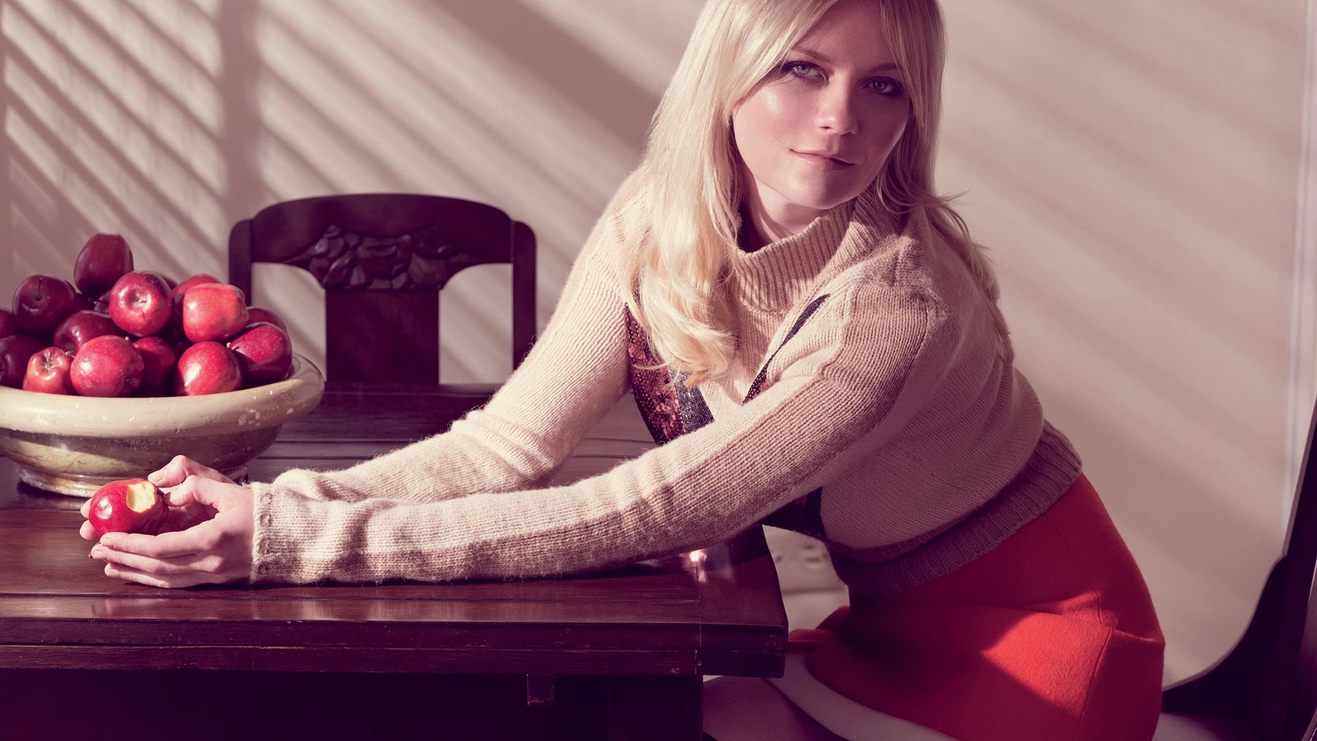 Kirsten Dunst sitting on a dining table while holding an apple