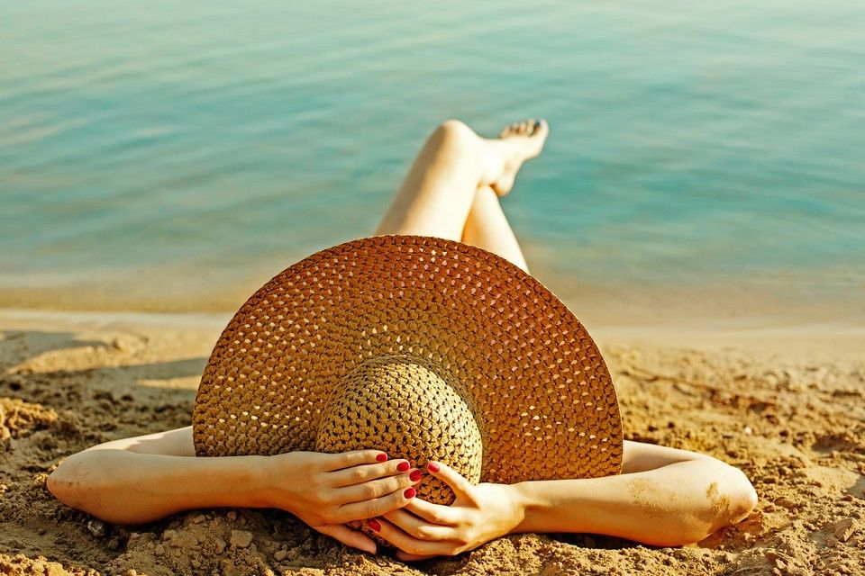 A woman wearing a straw hat and relaxing on the beach