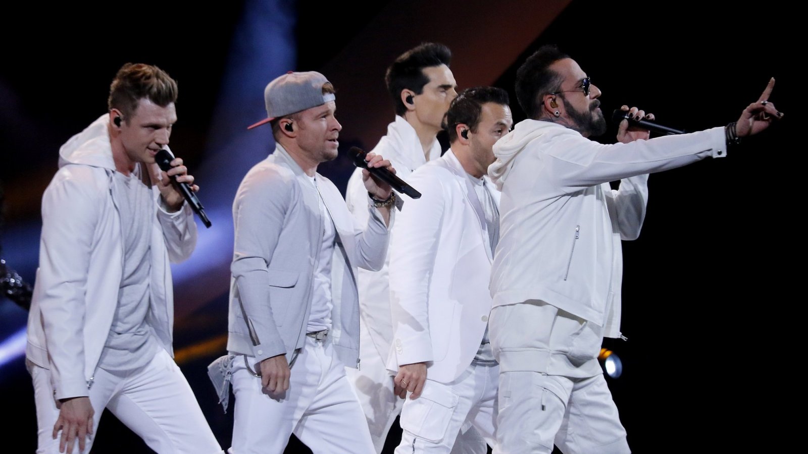 Backstreet Boys wearing white outfits while holding microphones
