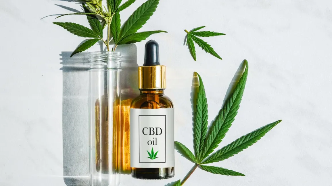 Glass bottles labeled as CBD oil and some hemp leaves are present in glass while other outside.