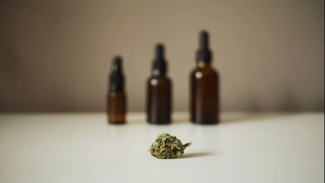 A cannabis leaf with three closed brown tincture bottles of different sizes blurred in the background