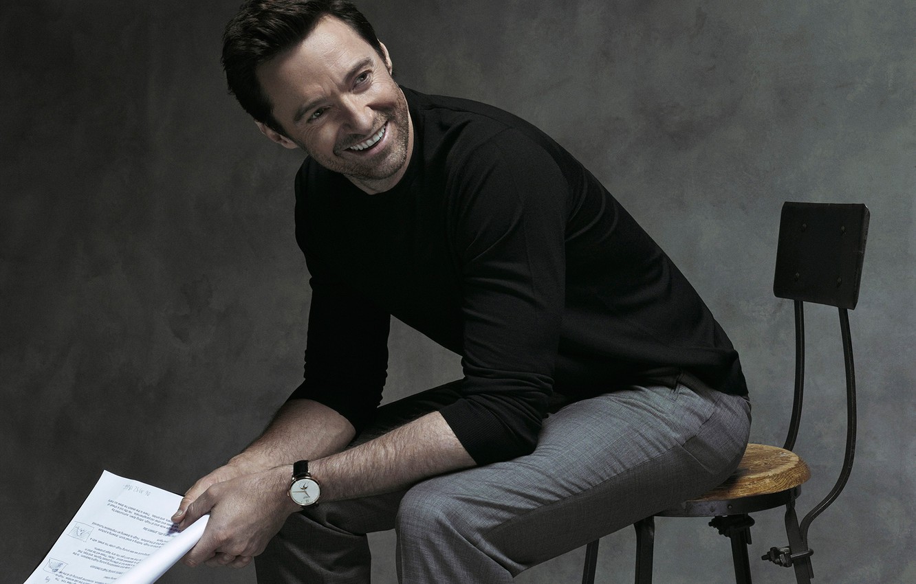 Hugh Jackman wearing a black sweater while sitting and holding a paper