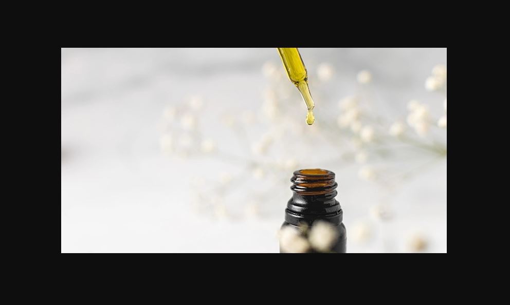 A dropper dropping CBD oil into an open brown bottle