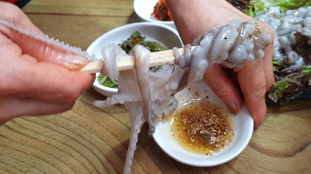 Person's hand using chopsticks to eat Sannakji