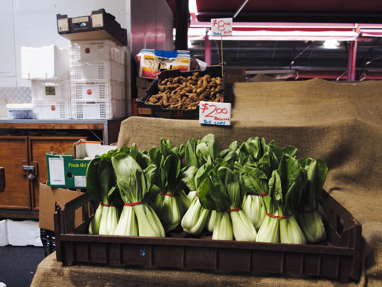 Several tied bok choy by twos on a plastic brown tray in a market and sold for $2 per bunch