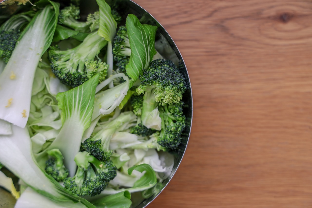 Top view of a bok choy and broccoli salad on a round container on a wooden brown surface