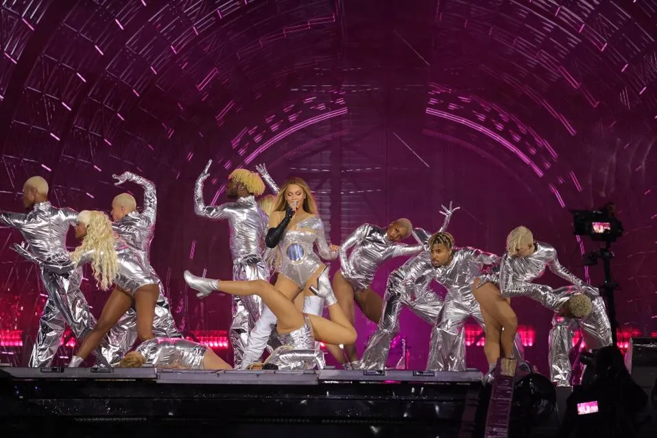 Beyoncé performing on stage with backup dancers, all dressed in shiny metallic outfits, in the midst of an energetic dance routine.