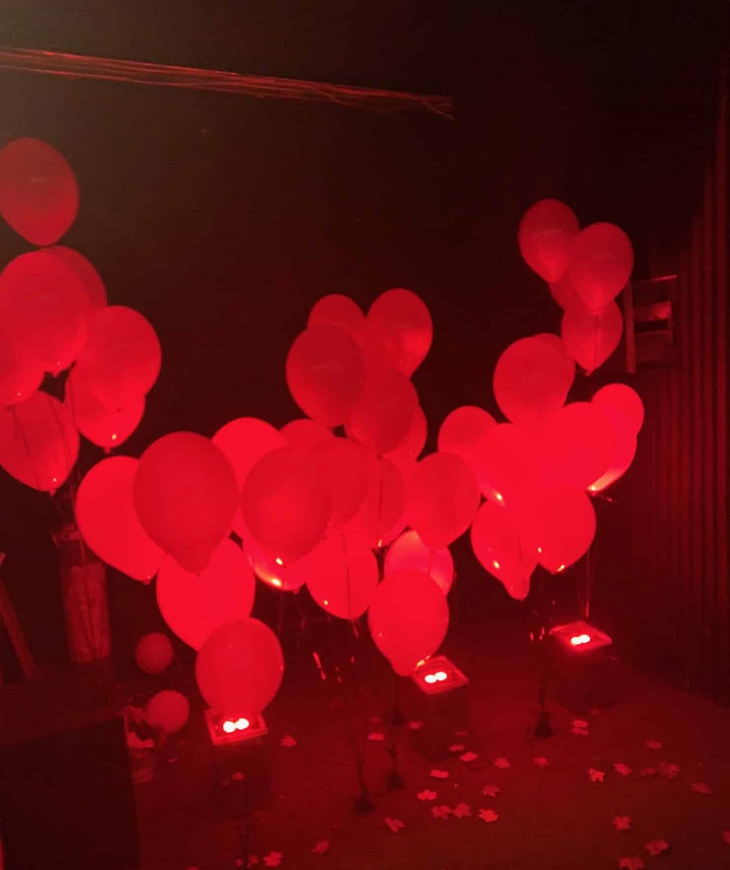 Dozens of white balloons with strings attached to the ground in a red-lit room at Pennywise Fun House in London