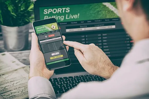 A man is watching live betting on mobile phone and laptop.